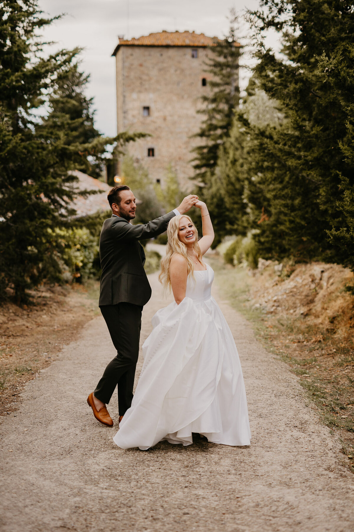 Bride and groom dancing joyfully in front of Ristonchi Castle, elegant wedding photographer Florence Tuscany.
