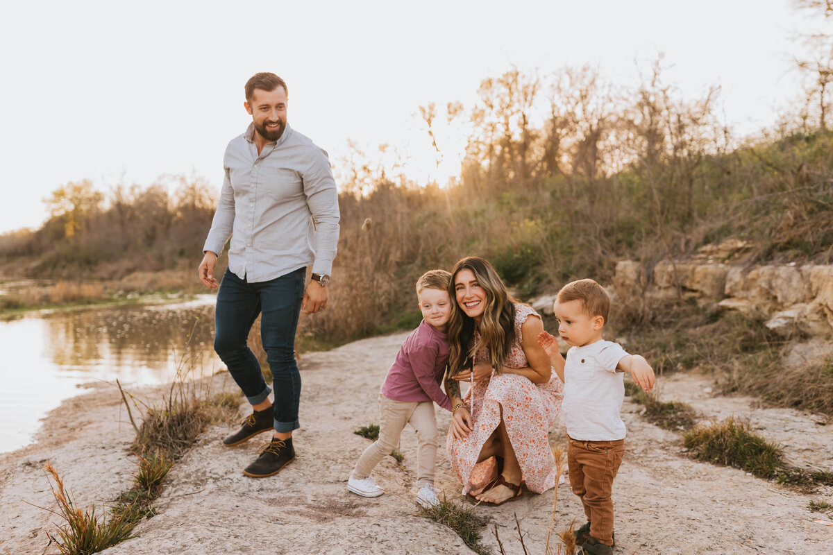 A family with two young boys hugging their mother by the lake