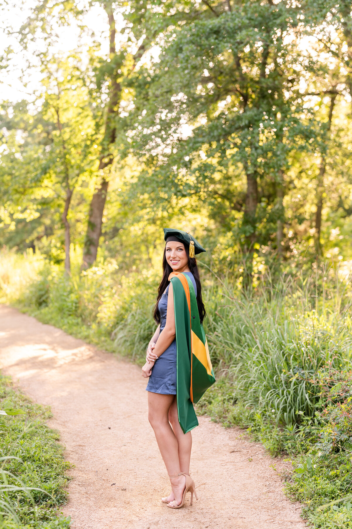 Baylor senior girl smiling over shoulder and smiling while wearing doctorate hood and cap surrounded by nature at the Houston Arboretum