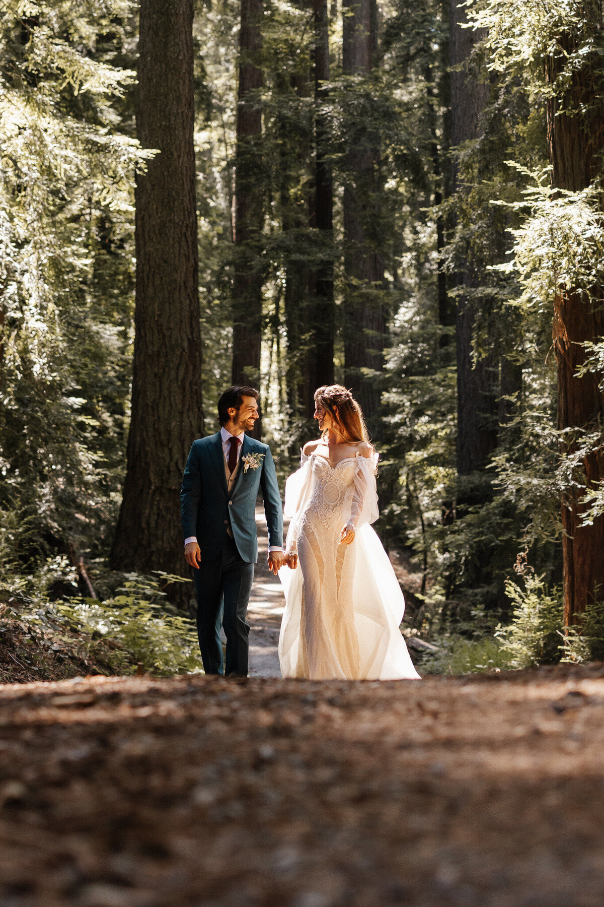 Bride and groom walking together through the redwood forest during their outdoor wedding, surrounded by tall trees and sunlight.