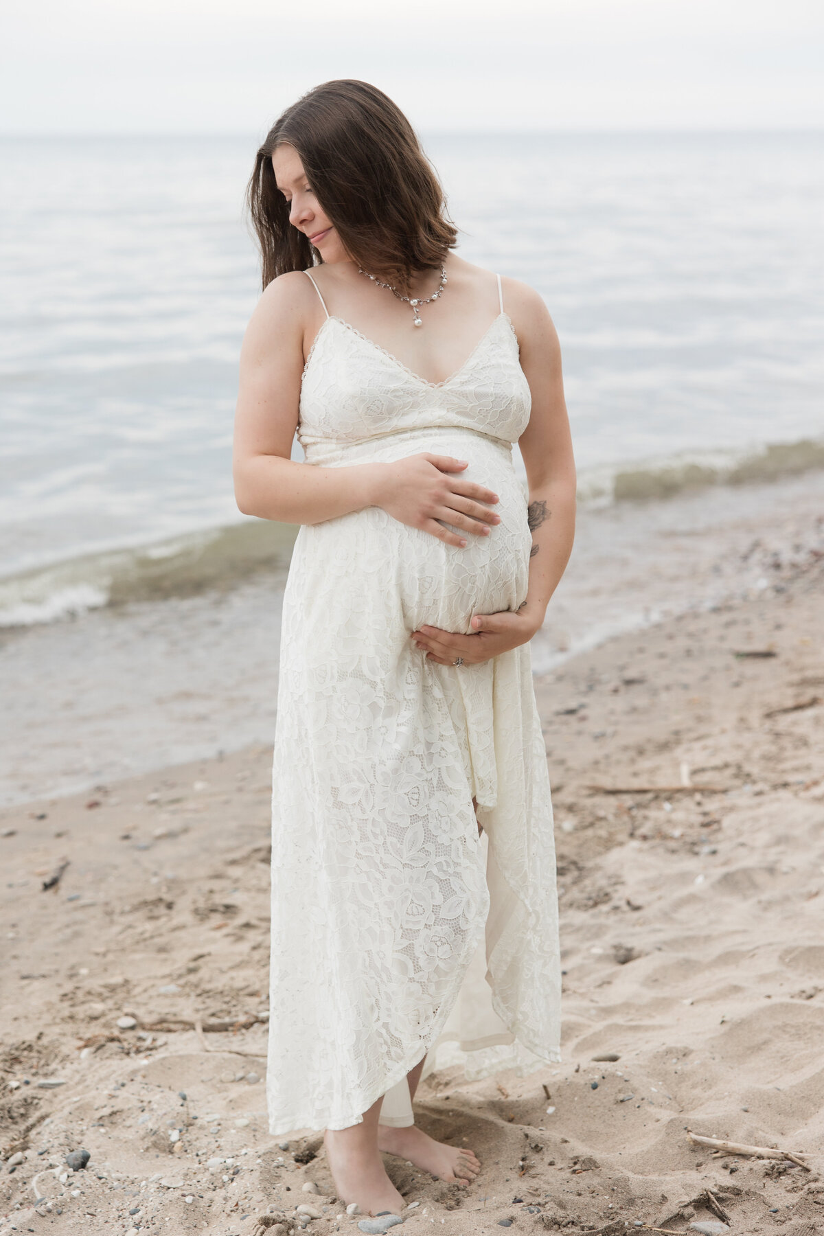 Expectant mother holding her baby bump on the beach and looking down over her shoulder