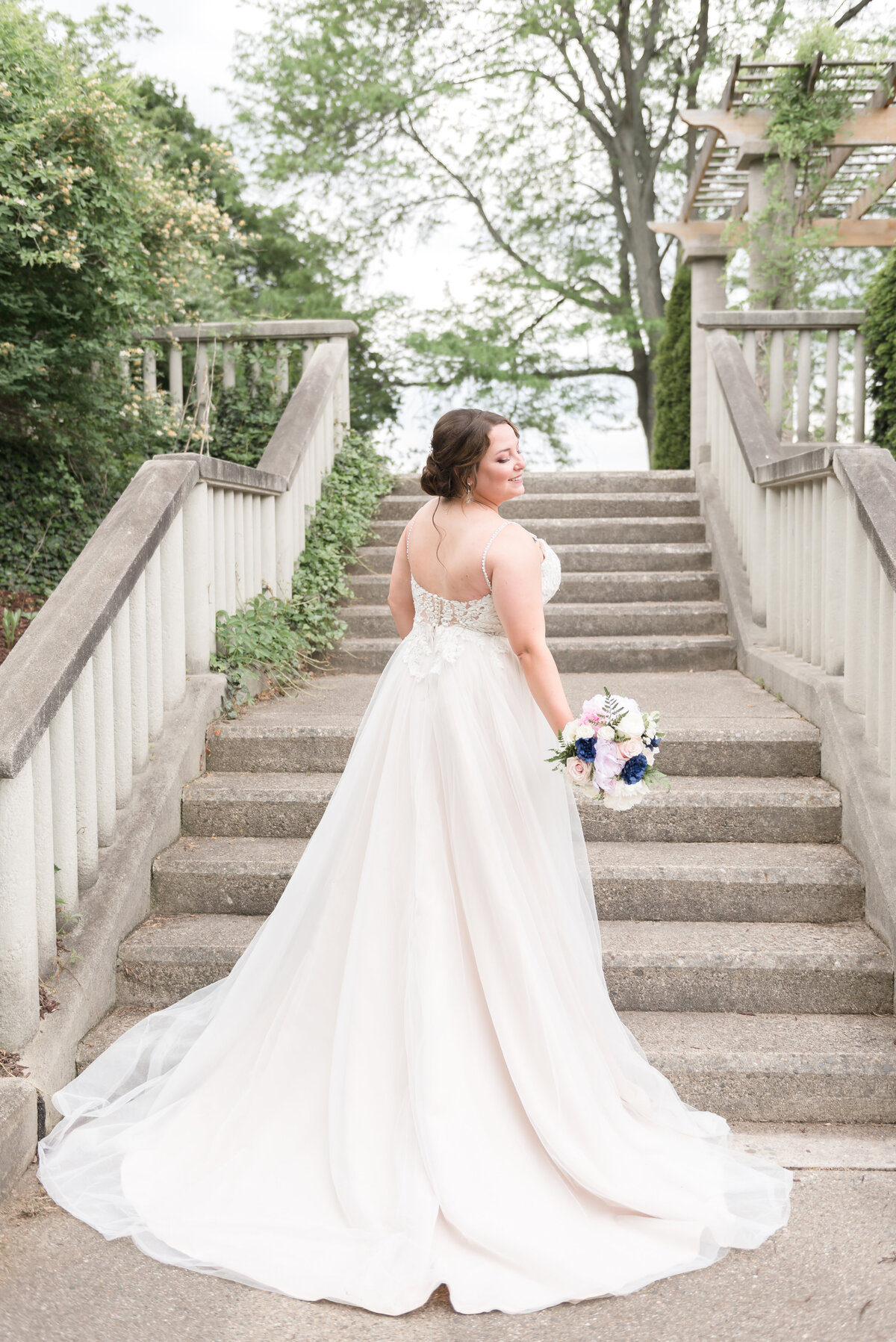 bride standing in front of steps looking back over her shoulder with her bouquet in her hand