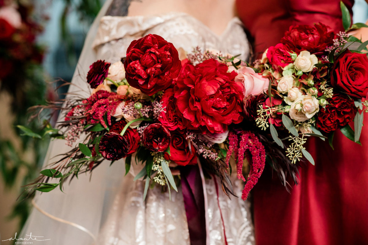 Winter bridal bouquet of deep red peonies, red roses, ranunculus, and red ribbon streamers