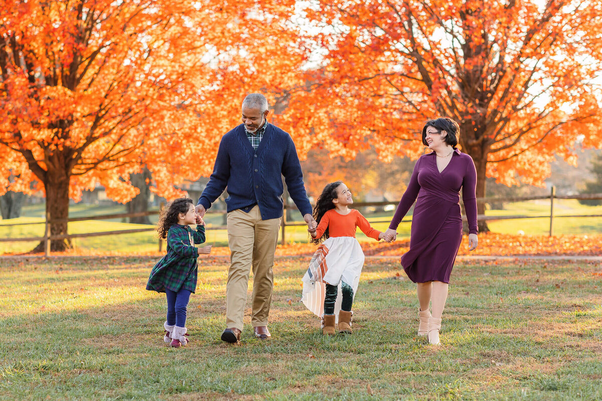 A family of four walking towards the camera with bright orange fall trees behind them.
