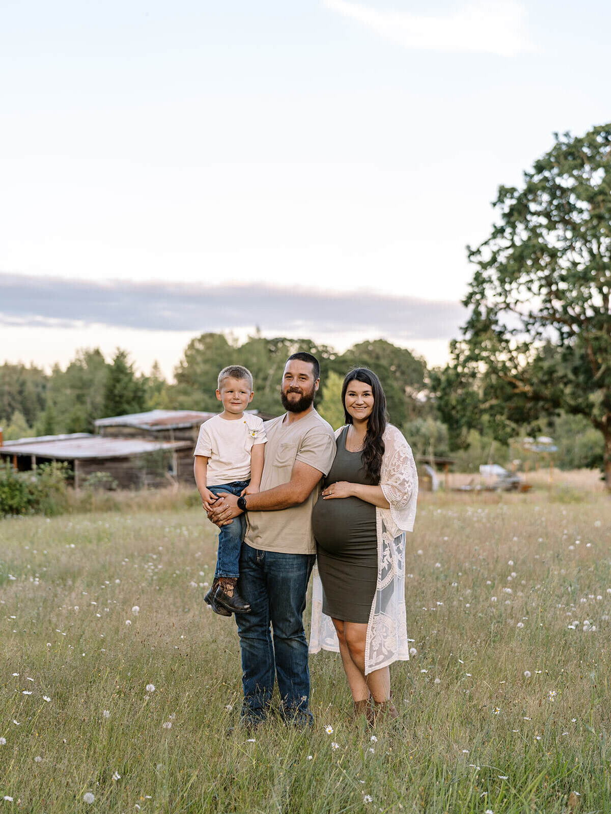 A couple and their son smile at the camera while standing outdoors in a field.