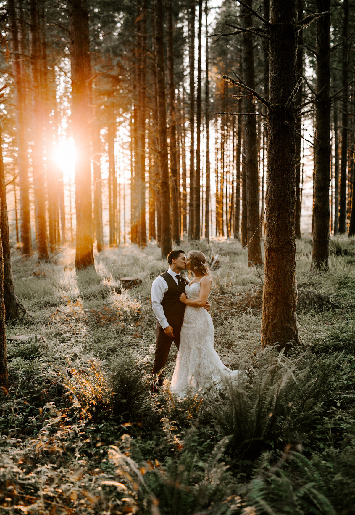 Couple kissing in a fern covered wood after their wedding at sunset