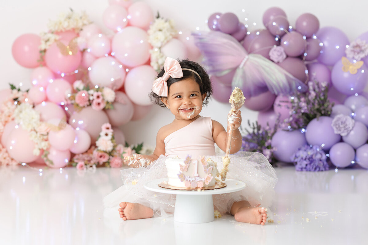 One year old Tampa baby girl enjoying a personalized luxury cake smash session with pink and purple floral decorations