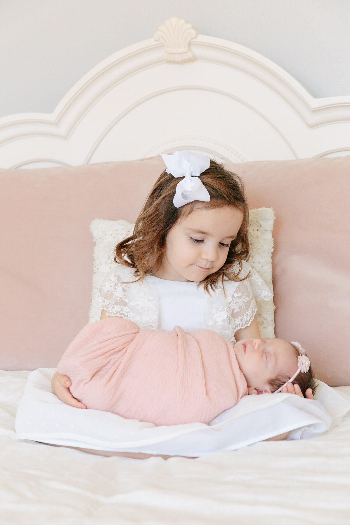 A small girl sitting on a bed holding a newborn