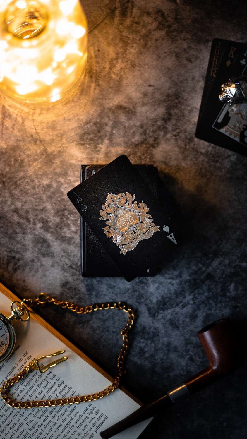 Black and gold ace of spades next to gold pocket watch, smokers pipe and open book