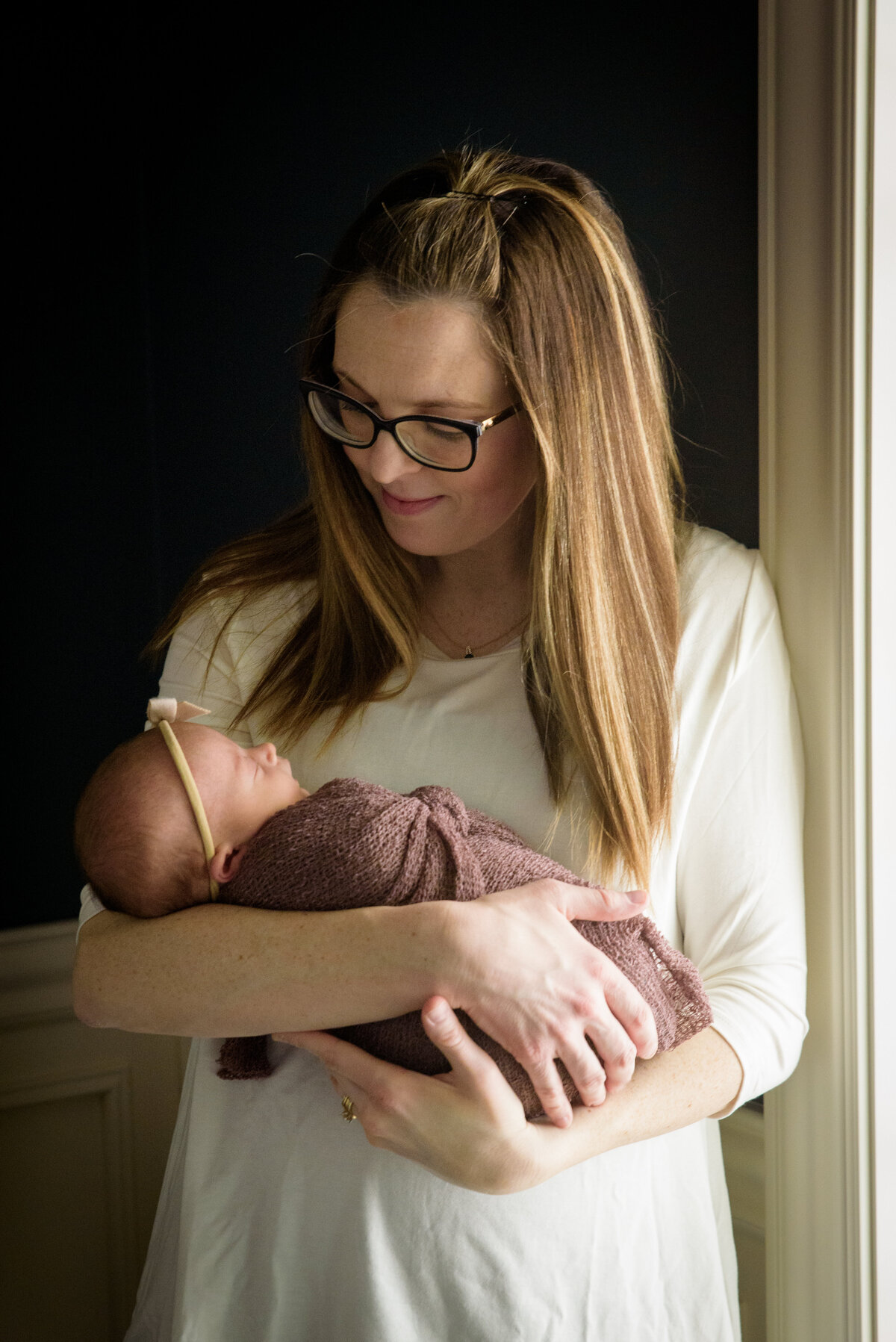 Beautiful mother holding new baby girl in a dusty rose wrap in natural light in their home in Green Bay, Wisconsin.