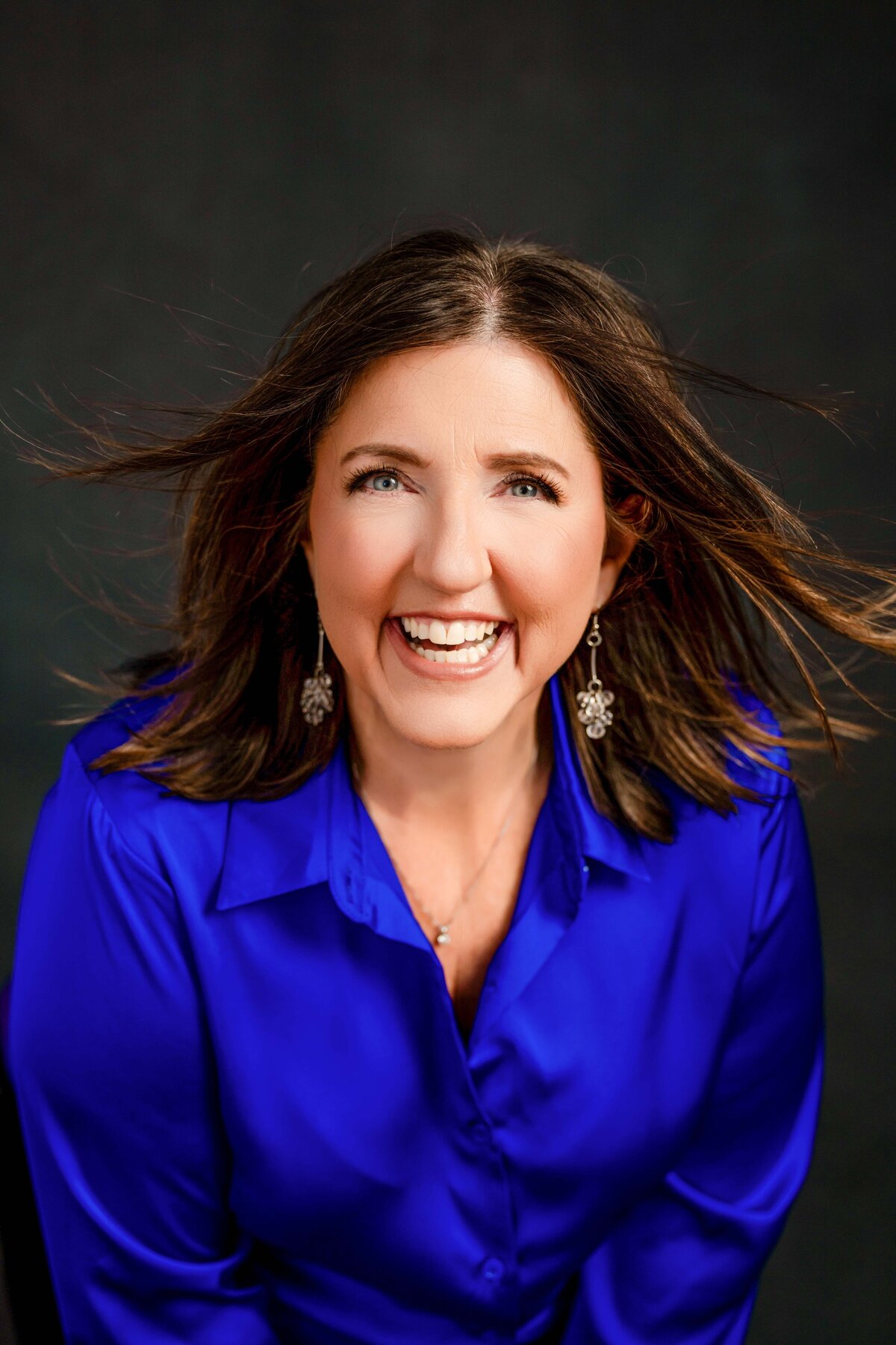 Vibrant branding headshot of a woman in a royal blue blouse, laughing confidently in the studio.