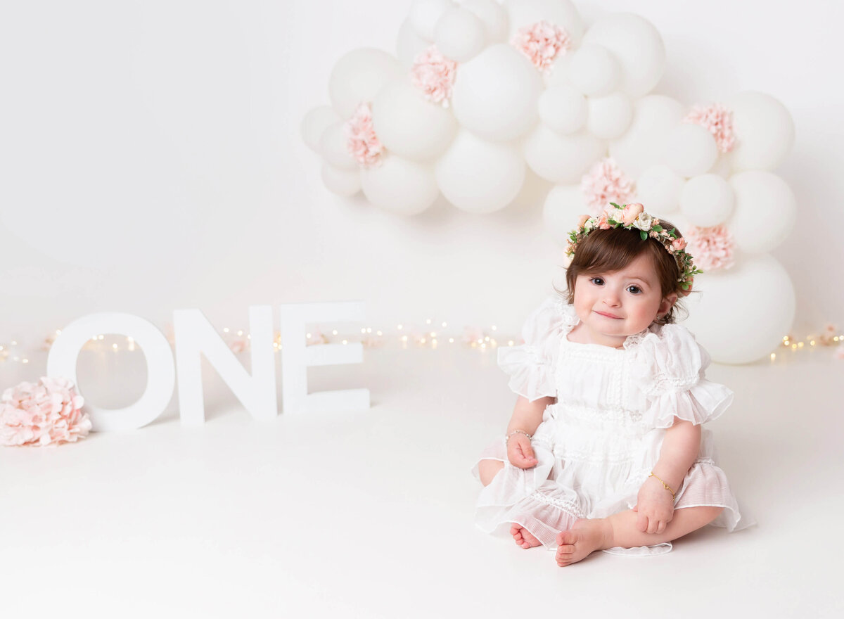 Top cake smash photographer NYC baby girl in white pink flower set up captured by Rochel Konik photography