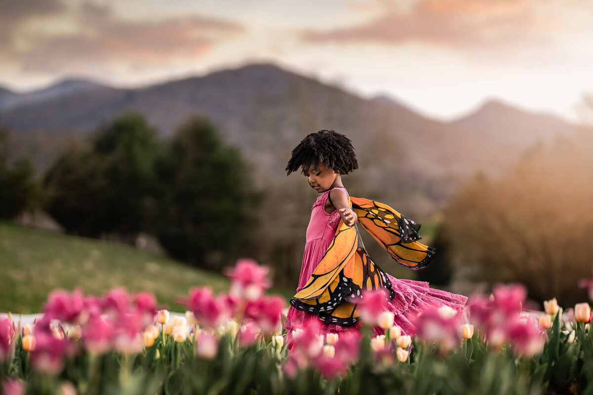 A young girl in a pink dress and butterfly wings twirls in the tulips near Asheville NC