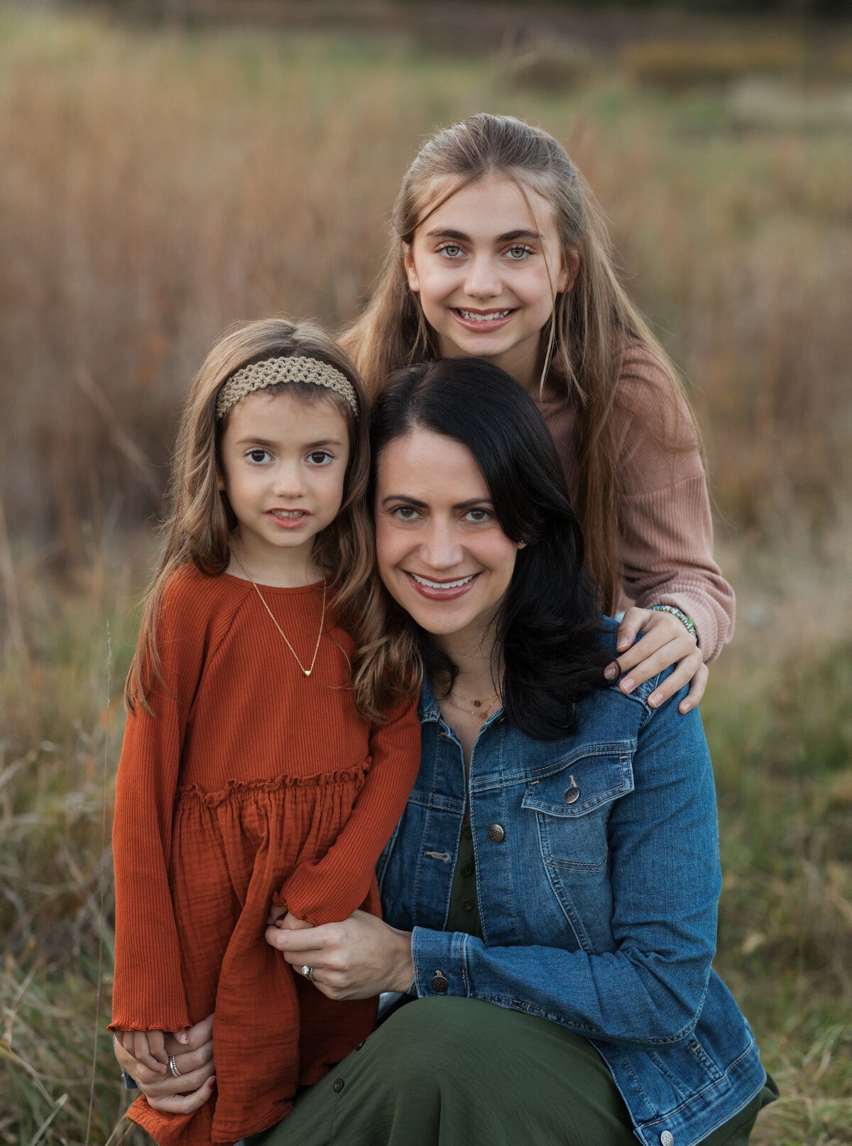 mom and two daughters sitting in field for family photos