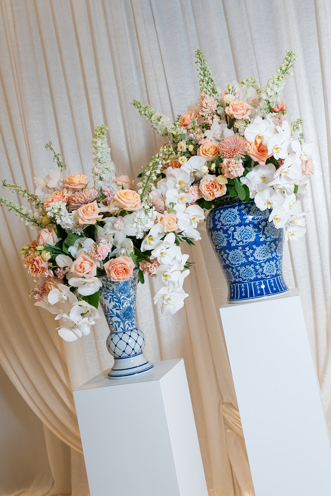 Blue chinoiserie vases filled with vibrant blooms on pillars framing the wedding ceremony at National Museum of Women in the Arts. 