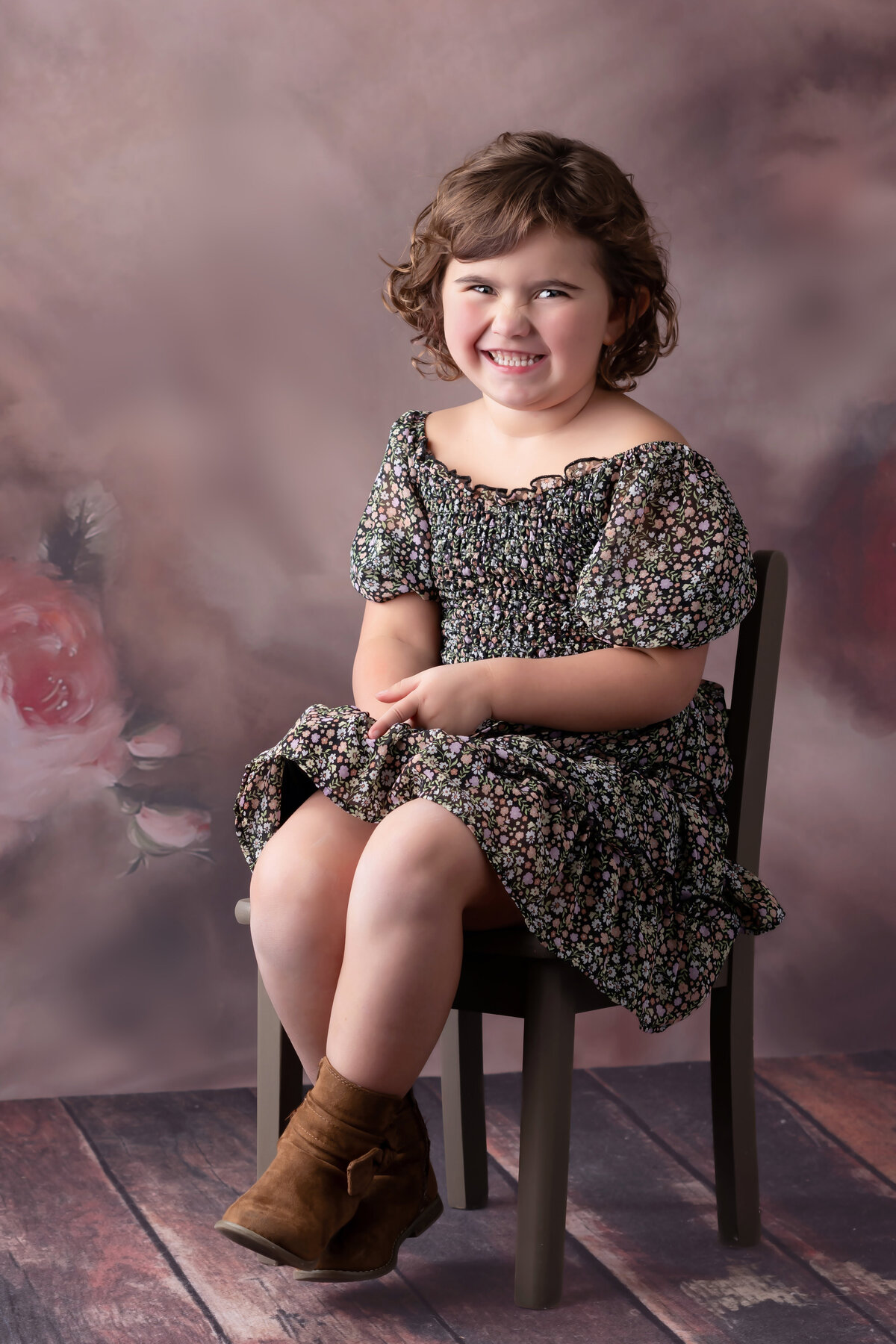 Young girl sits in a chair in a floral dress on a floral background.