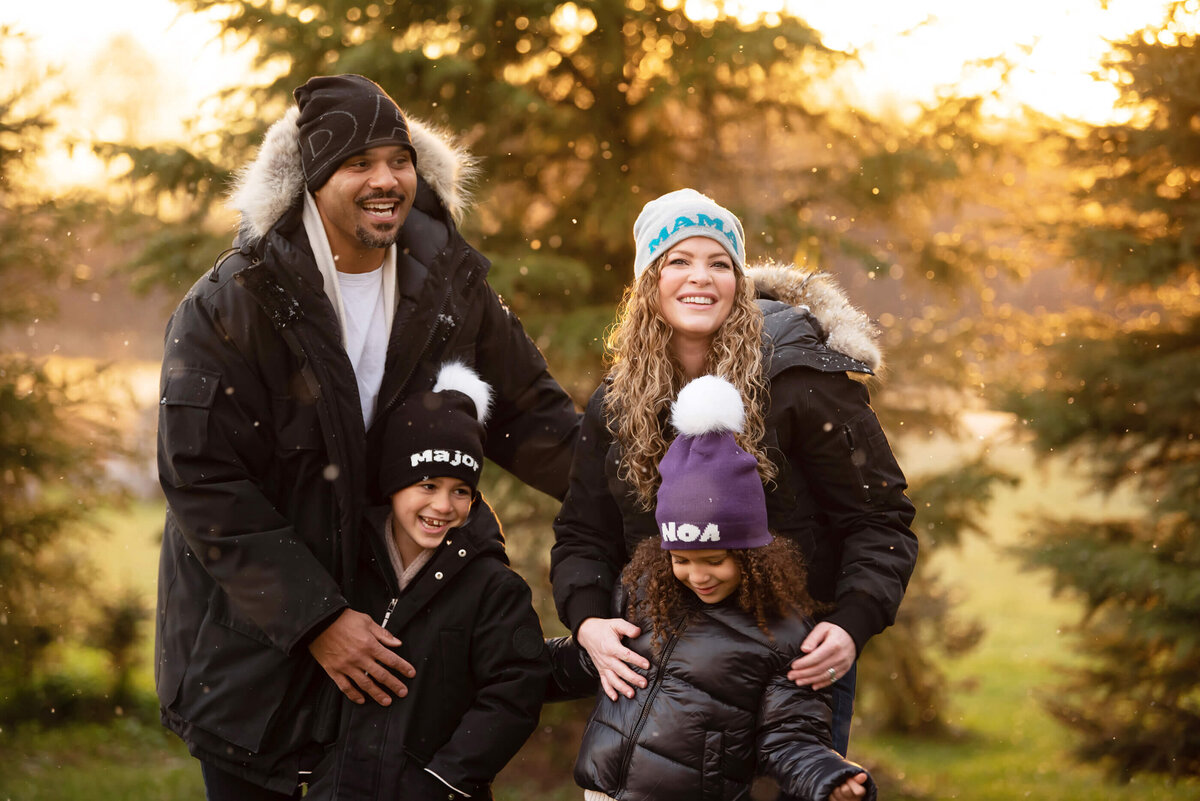 Mom and dad with their son and daughter all wearing beanies in the golden light for the winter family photos in Burlington, On