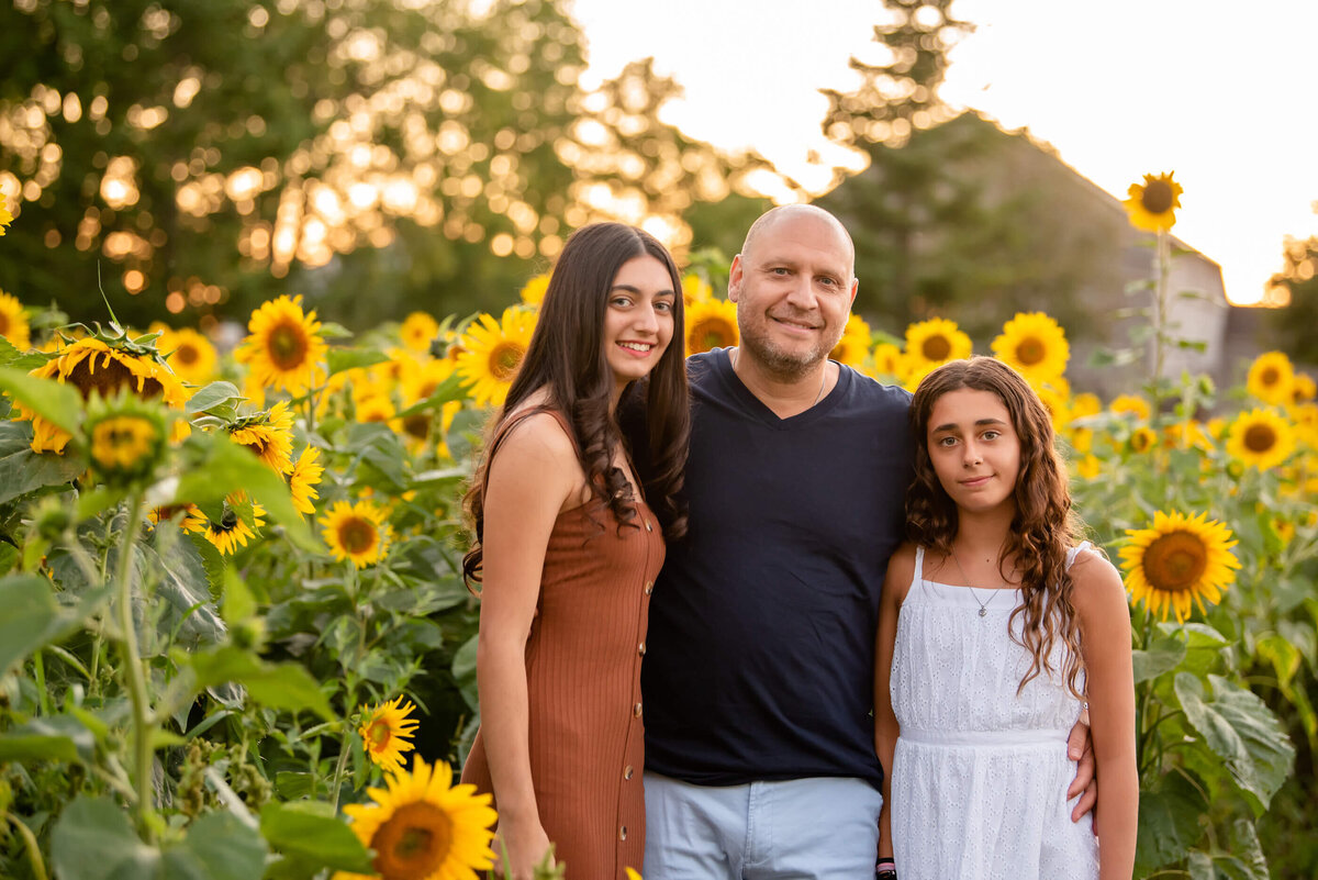 dad standing with his teenage daughters for their sunflower family photos in Burlington