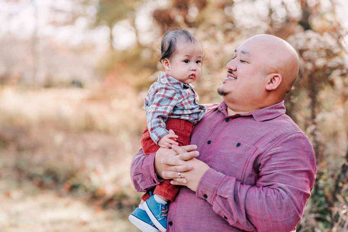 A bald man holding his 8 month old son by a northern virginia family photograher