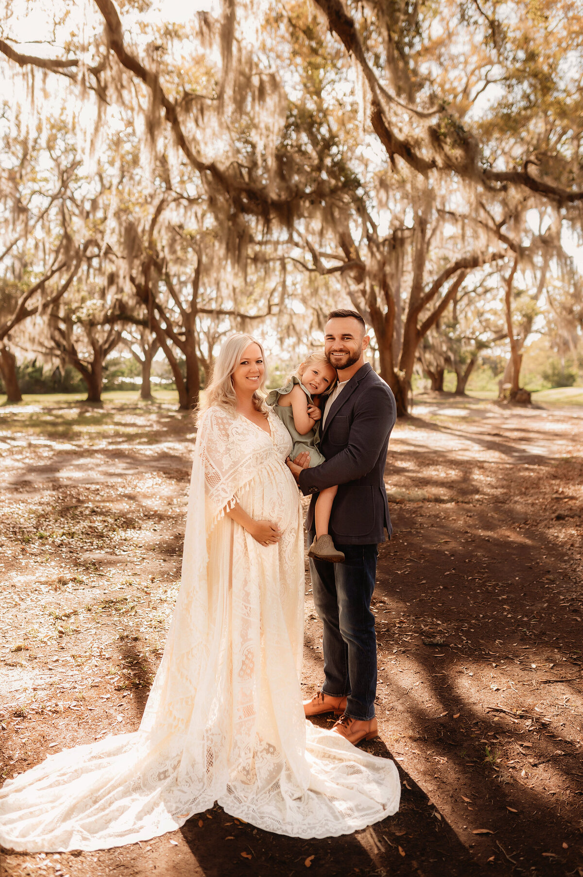 Family poses for Maternity Photos with oak trees in Charleston, South Carolina.