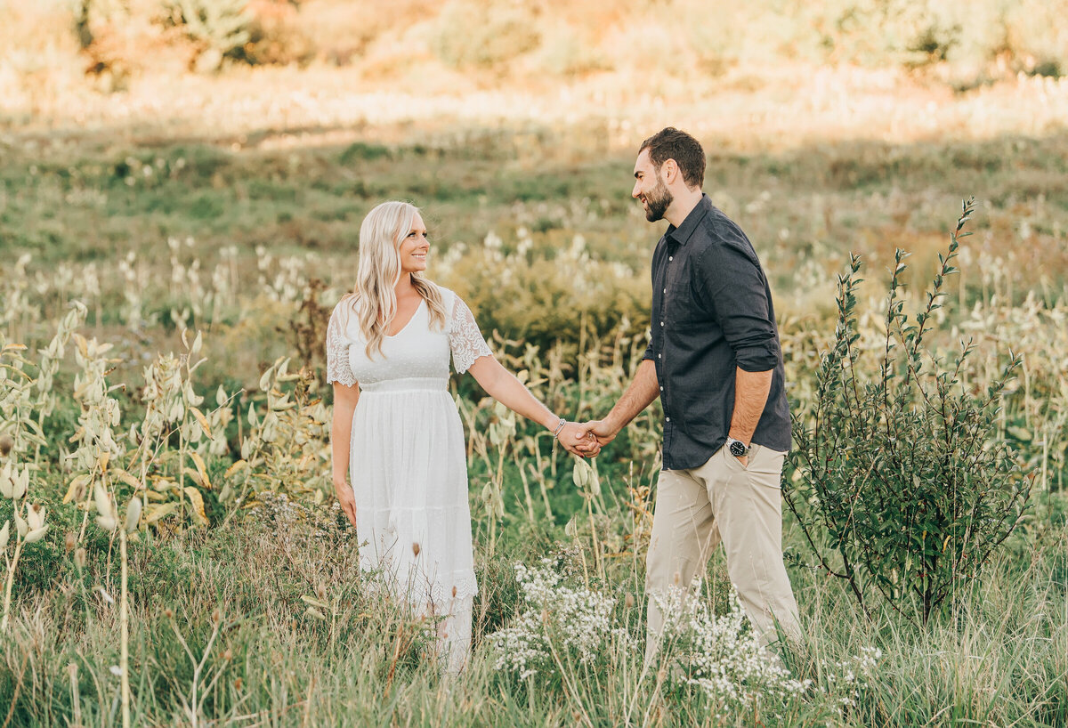 Couple walking in a field at their Summer engagement session in London Ontario