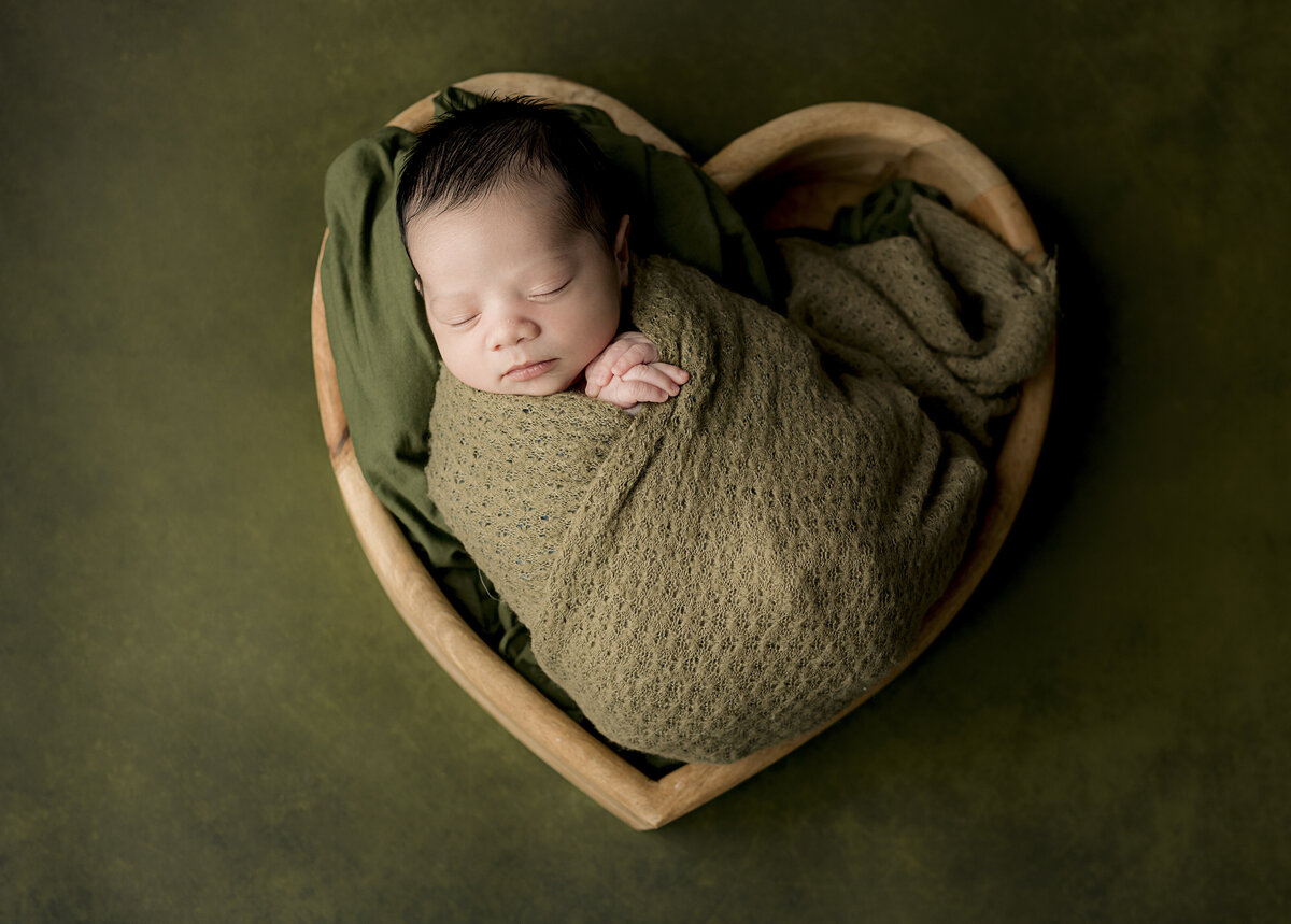 baby in heart basket on green backdrop