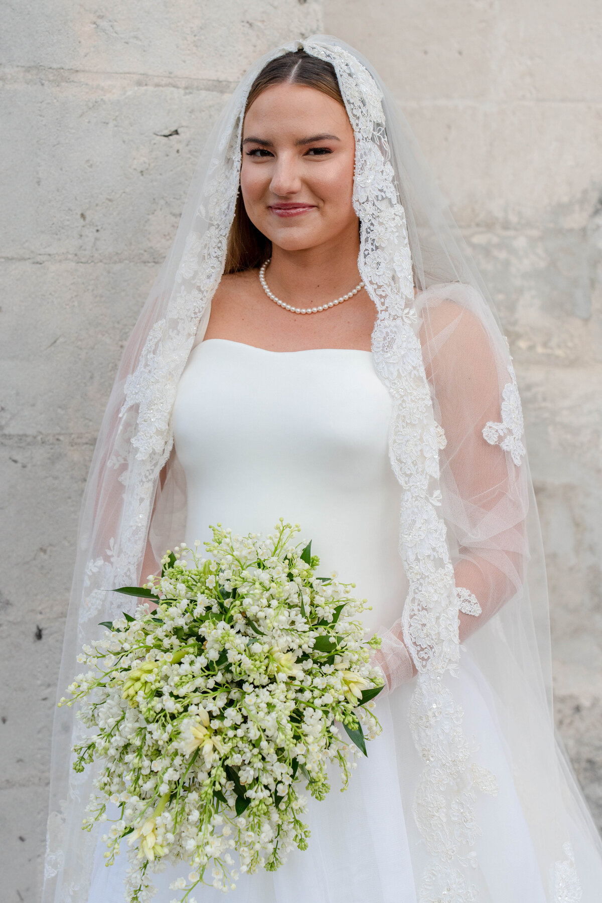 Bride wearing an elegant wedding gown with a lace veil, holding a lush white floral bouquet at a luxury destination wedding in the Bahamas, captured by Mari Harsan Studios.