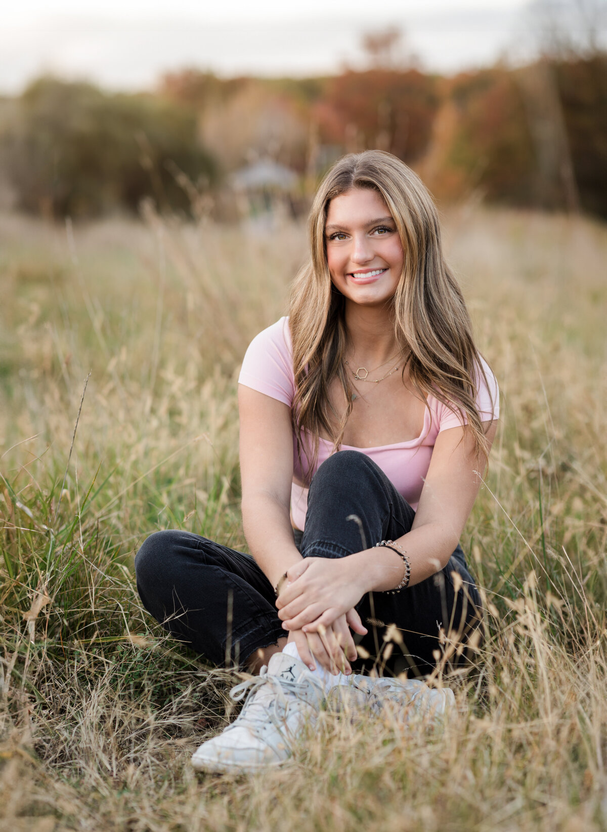 senior girl in pink top posing for senior photos in field Cleveland senior photographer