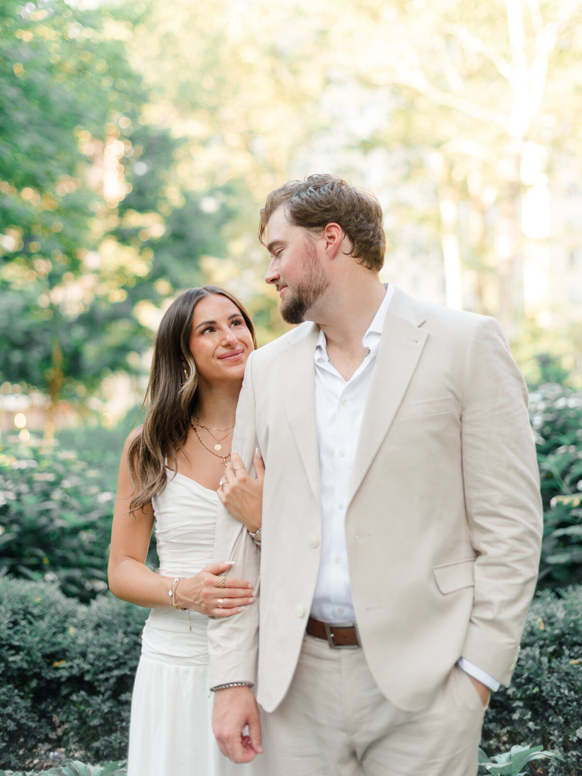 A couple shares a tender moment in Rittenhouse Square, the bride-to-be gazing lovingly at her fiancé as they stroll through the garden path. Surrounded by soft greenery and golden afternoon light, their connection feels timeless and genuine. Captured by Elizabeth Kane Photography, a Luxury Philadelphia Wedding Photographer.