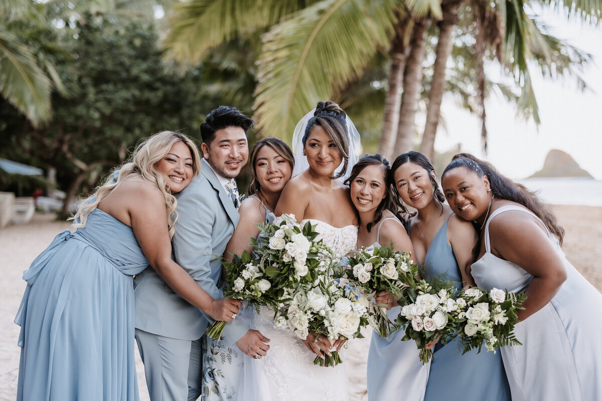 Bridesmaid and bridesman portraits wearing shades of blue holding bouquets on the beach with palm trees behind