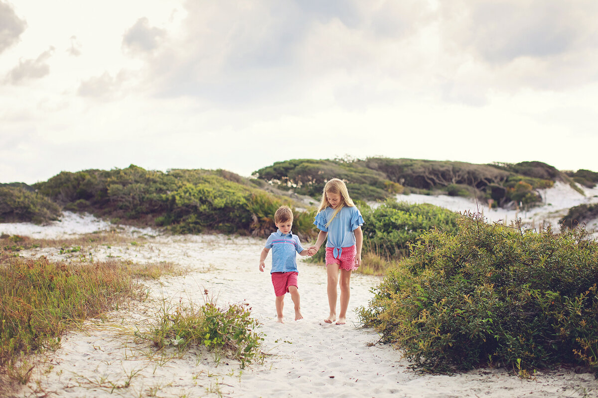 brother and sister walking hand in hand on trail at grayton beach state park, florida. 