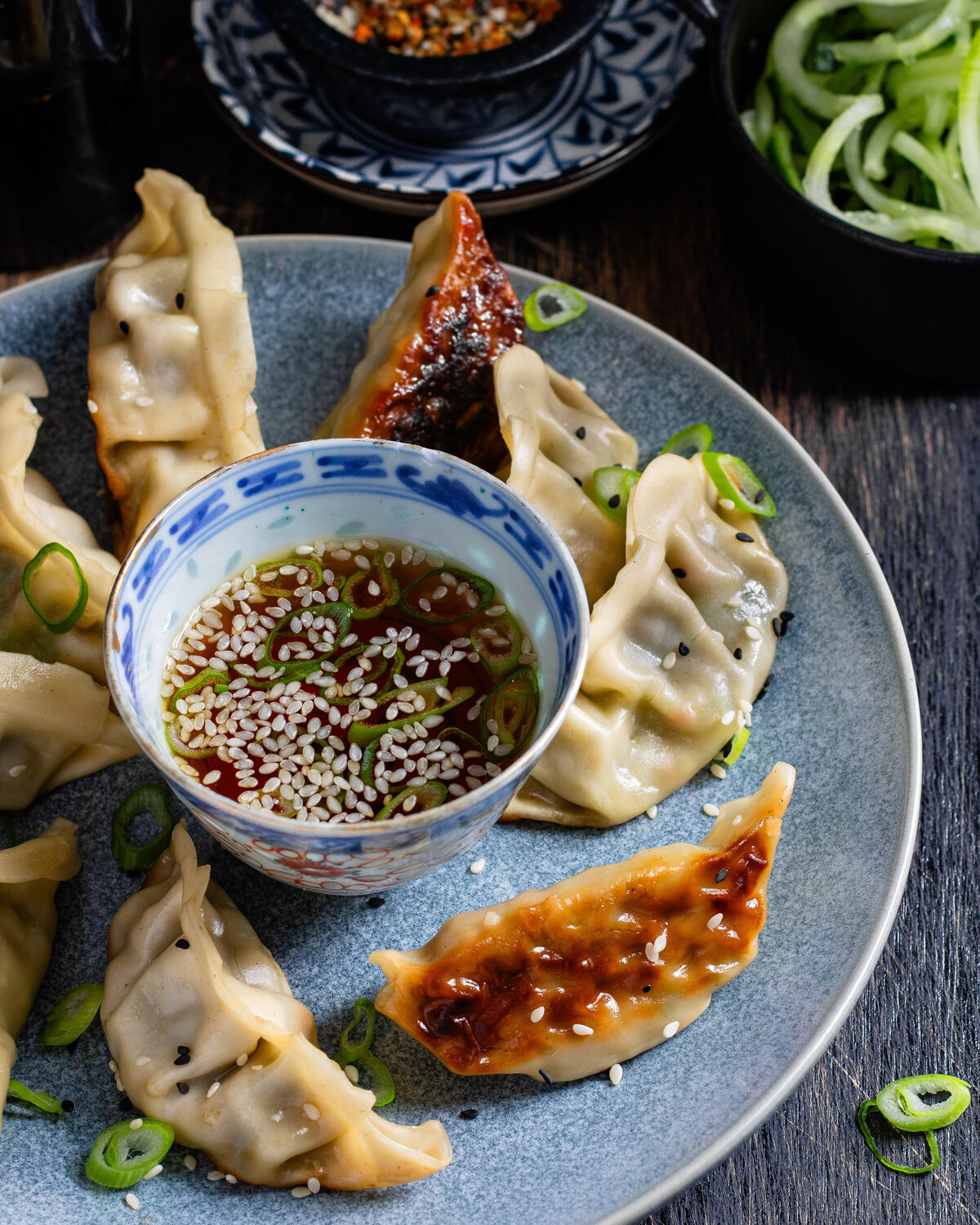 Vegetable Gyozas around a dip bowl on a plate with spring onion garnish and sesame seeds