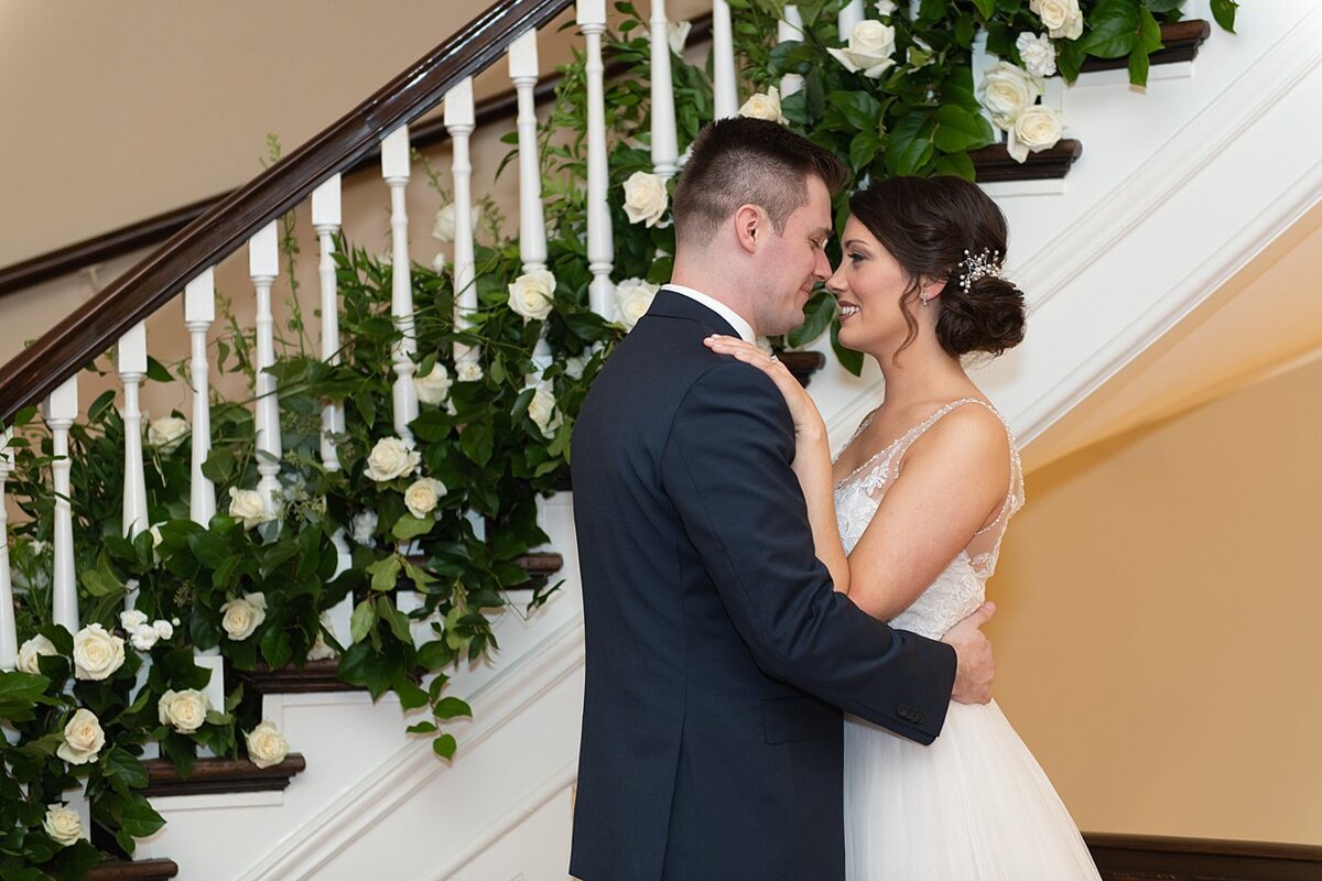 Bride and Groom sharing a private moment in front of a greenery and floral lined staircase at University Club in Pittsburgh, PA