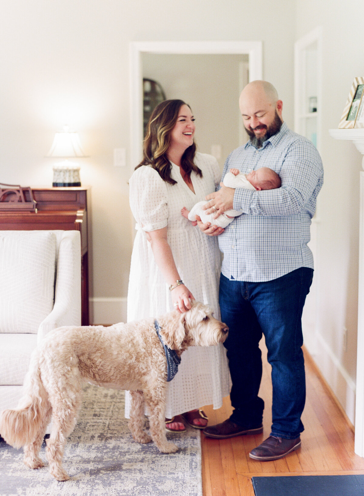 Family laughs as they hold their baby and pet their dog during an in home newborn session. Image by Raleigh newborn photographer A.J. Dunlap Photography.