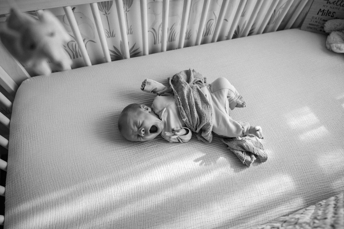 black and white photo of a newborn baby waking up in his crib