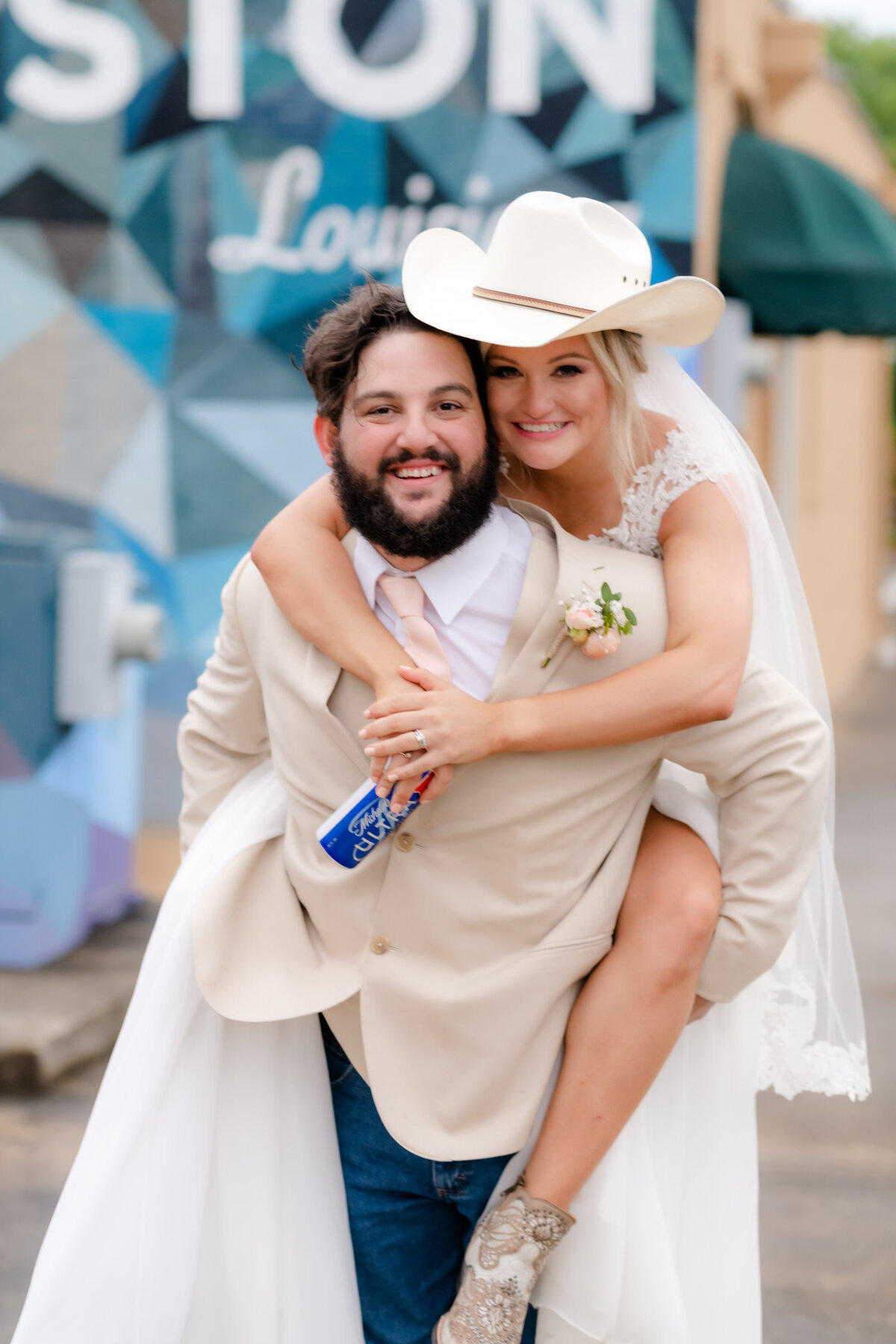 bride piggy backing on her groom while wearing his cowboy hat as they both smiles at the camera and Little Rock wedding photographer