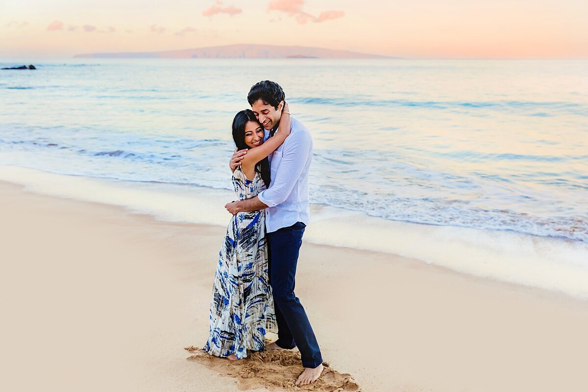 Woman puts her arms around the neck of her partner after his surprise proposal on a beach in Maui
