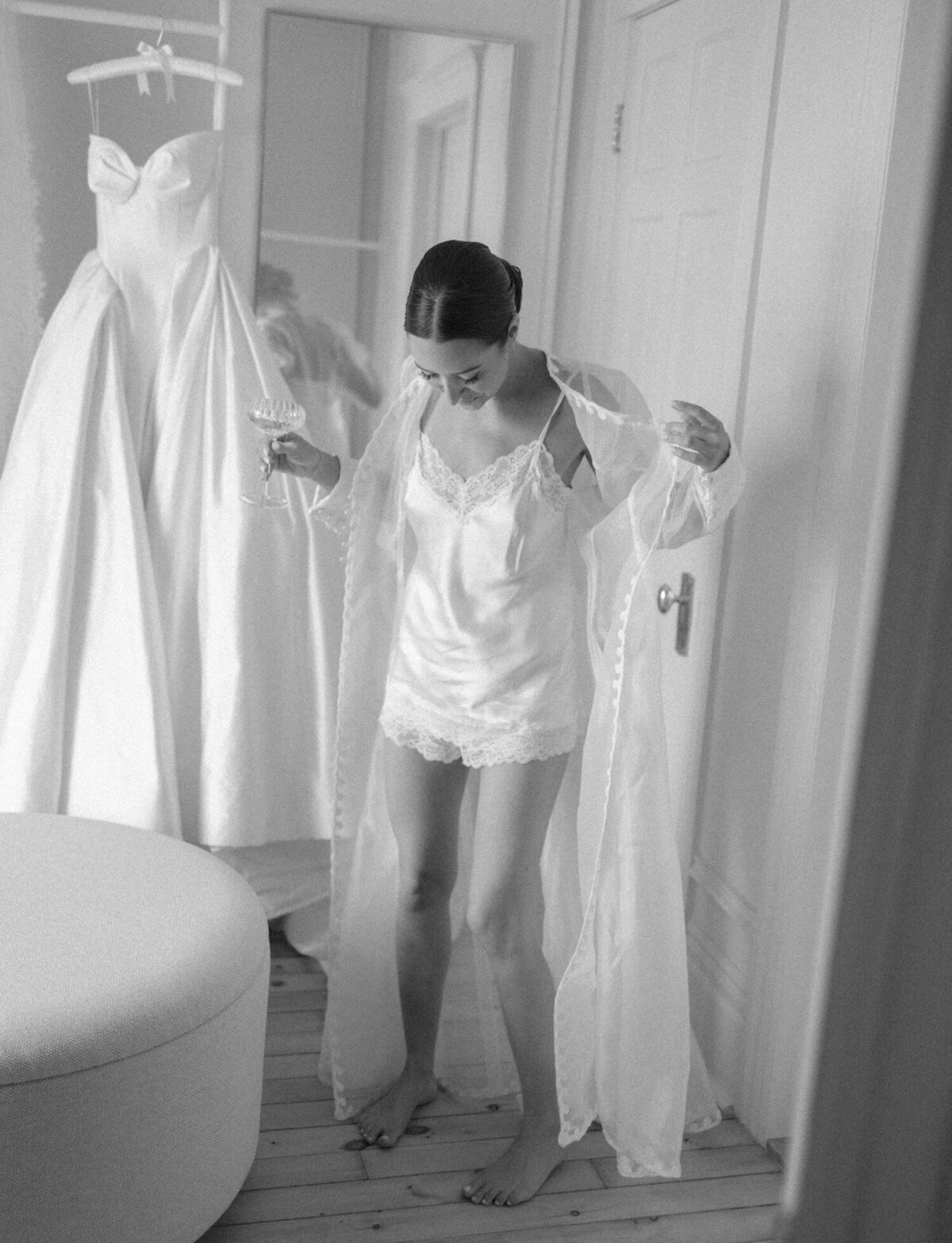 a bride in a silk & lace robe made from her mother's wedding dress holds a champagne coupe, just before slipping into her wedding dress at 1 room hotel in Detroit