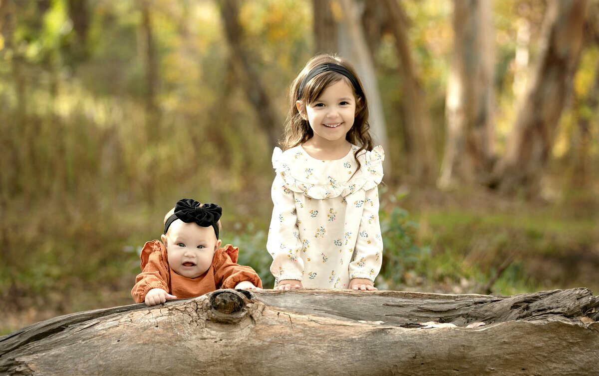 LITTLE GIRL AND BABY POSING ON A FALLEN TREE IN THE PARK