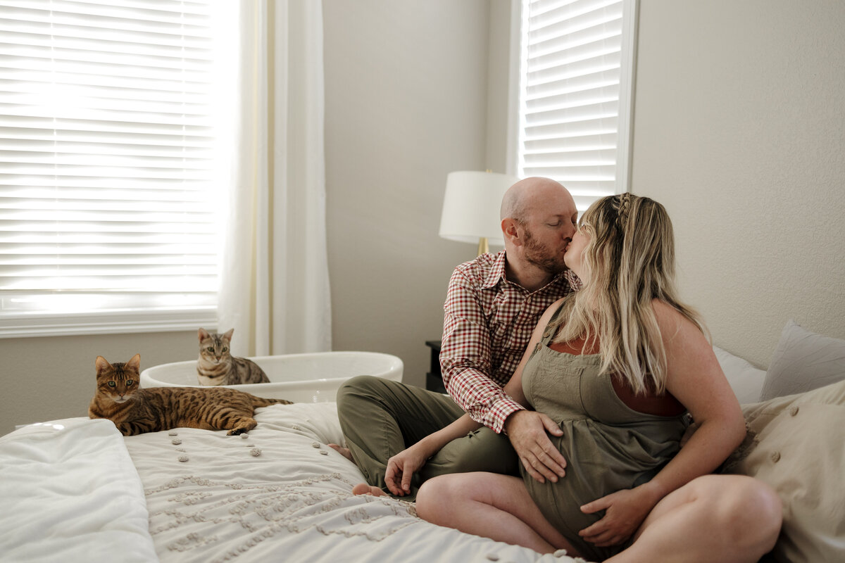 expectant-mom-and-dad-sitting-on-bed-kissing-at-home-in-longmont-colorado