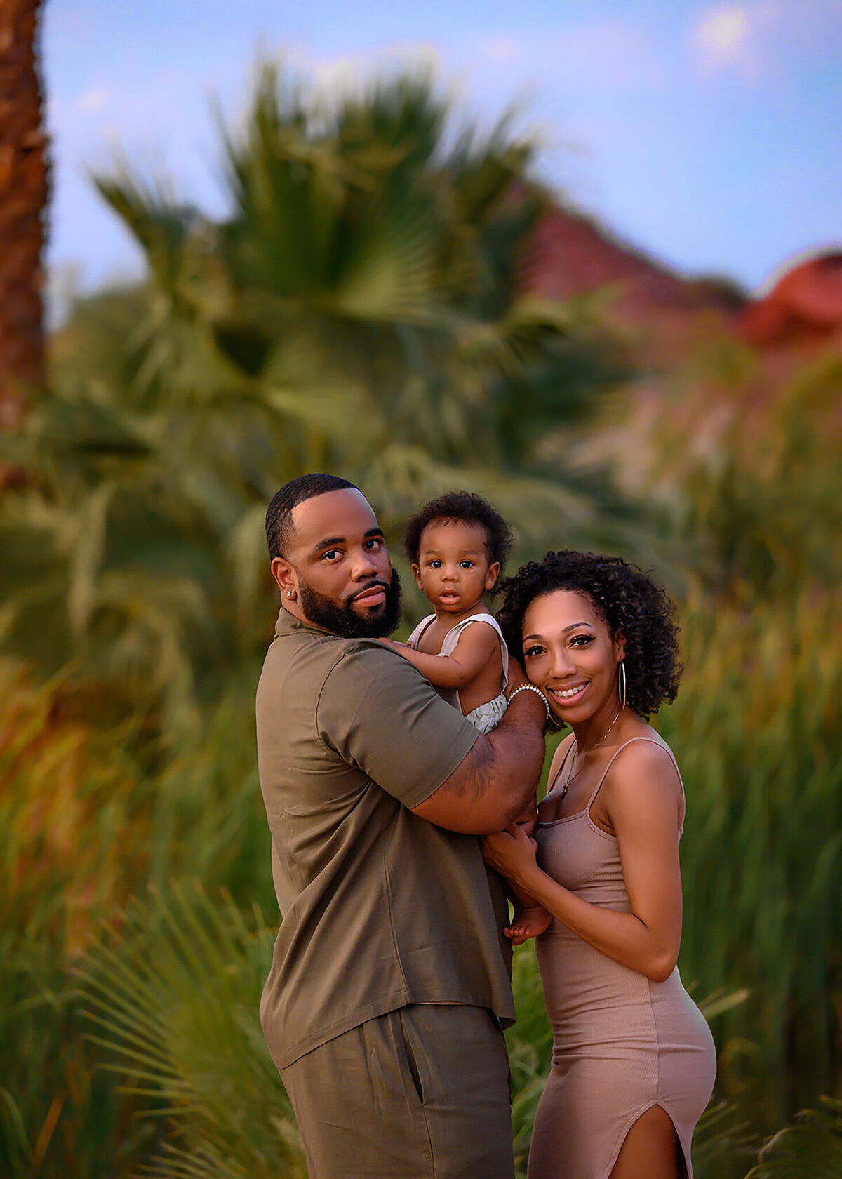 gorgeous family in light tan clothing with dad holding son and mom snuggled to them in front of a Hole in the Rock mountain in Phoenix