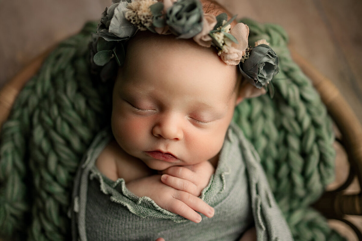 Fort Collins newborn photos with baby girl wrapped in green with flowers on her head
