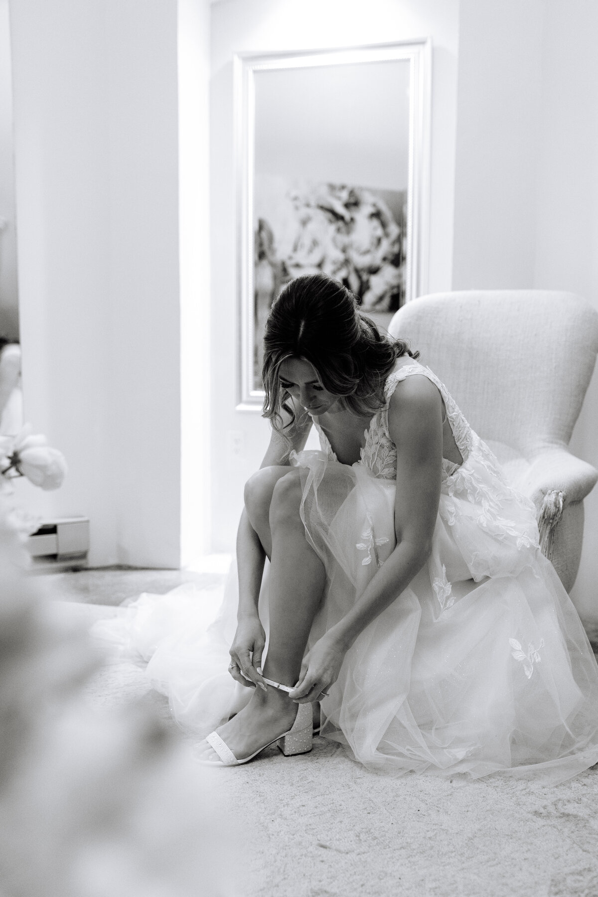 black and white image of bride sitting and clasping her shoe strap.