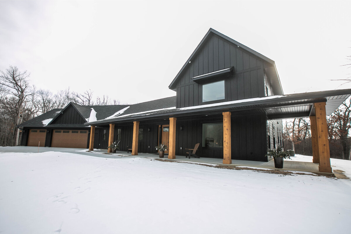 Exterior view of custom home in Elk River, Minnesota with black siding, wood details and front porch built by Cornerstone Custom Builds
