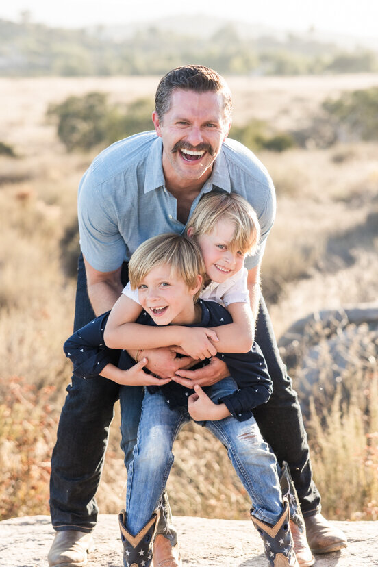 father-and-sons-laughing-together-family-of-four-sitting-on-rock-wrights-field-san-diego