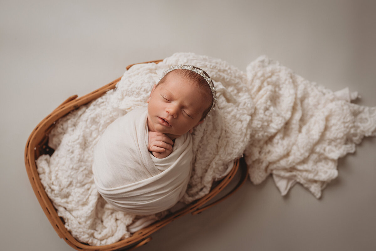 newborn baby girl at newborn portrait session in Woodstock, Georgia swaddled in cream laying on cream lace