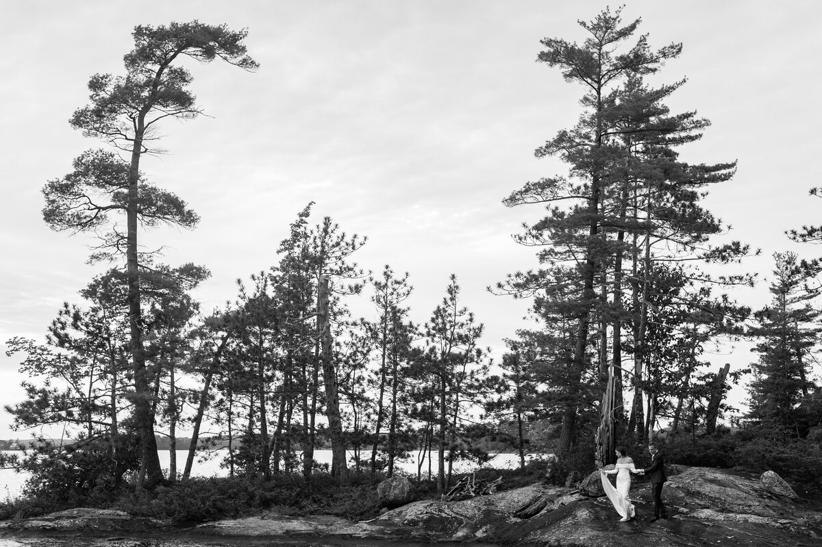 Couple in black and white walking along the shoreline of muskoka