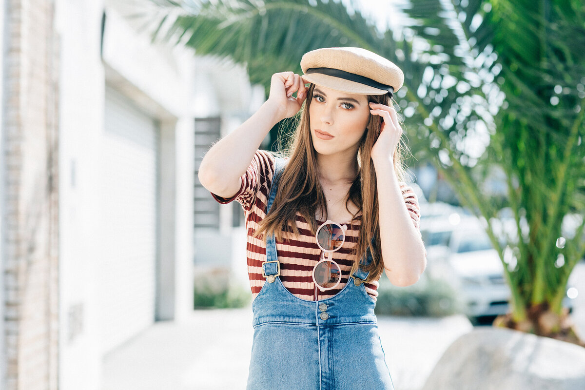 Senior girl rocking a vintage French vibe with a cream beret and striped top in front of a palm-lined alleyway.