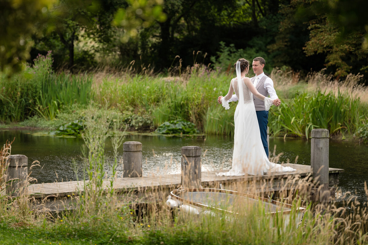 Bride and groom on a wooden jetty over a lake in an aboretum