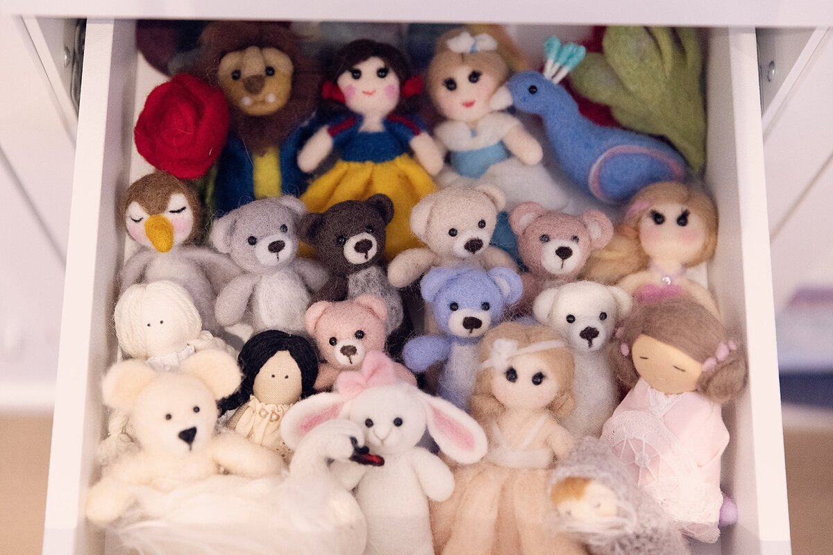 Drawer filled with neatly arranged stuffed animals and soft toys used as props in a newborn photography studio.